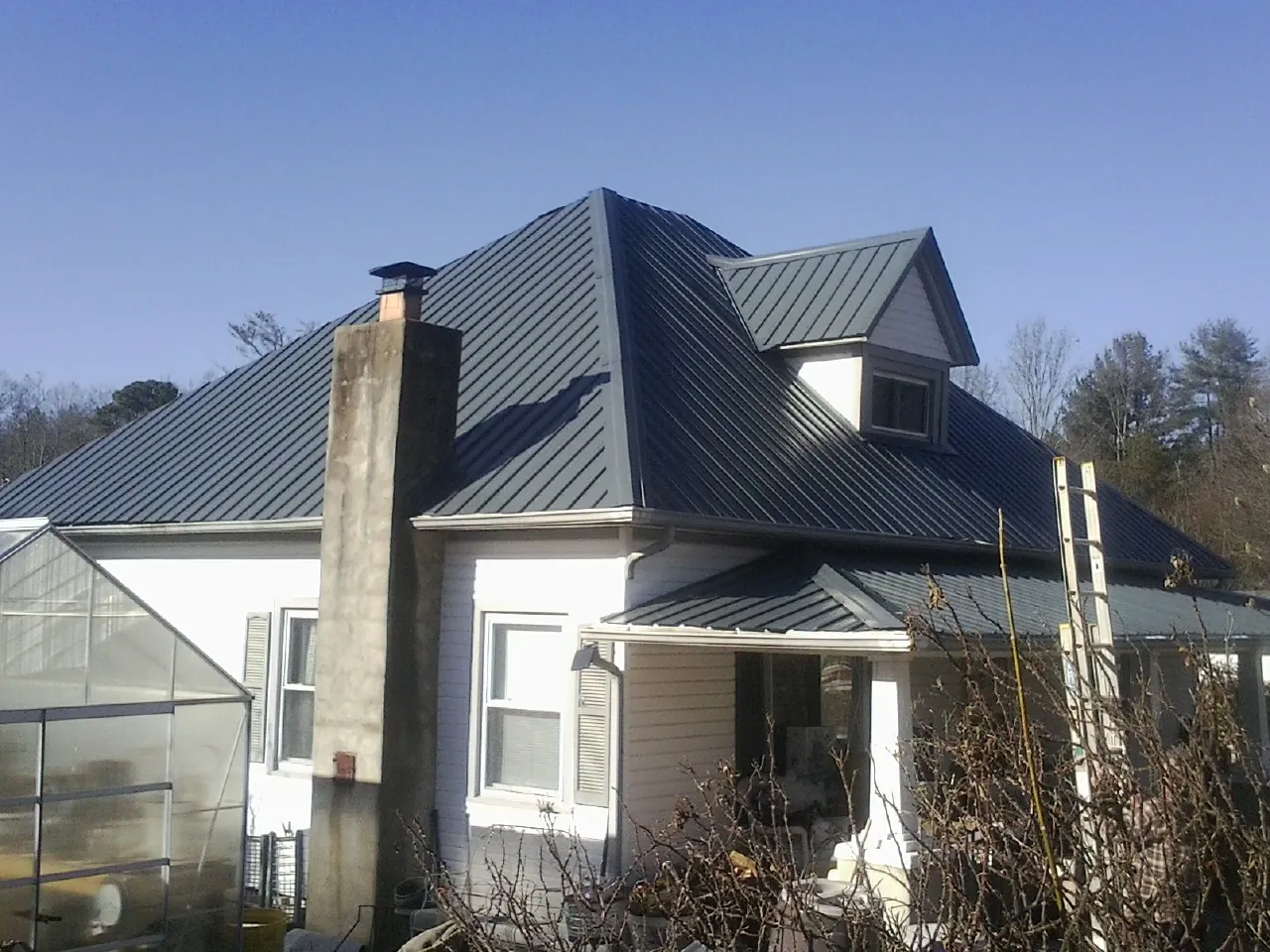 Dark blue standing seam metal roof on a white farmhouse with dormer — Slate & Tile Roof Repair by Roofing Brothers in Cranesville