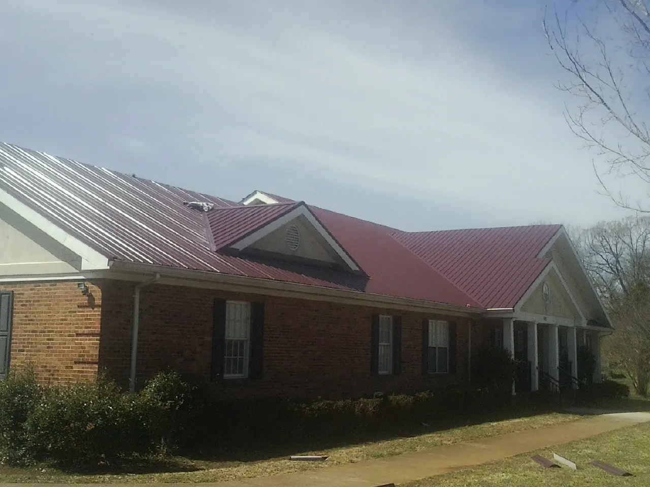 Red metal roof with gabled entries on a long brick building, from a Hail Damage Roof Repair job in Cranesville