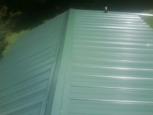 New green metal panels meeting at the ridge of a roof — Flat Roof Repair work by our crew in Cranesville