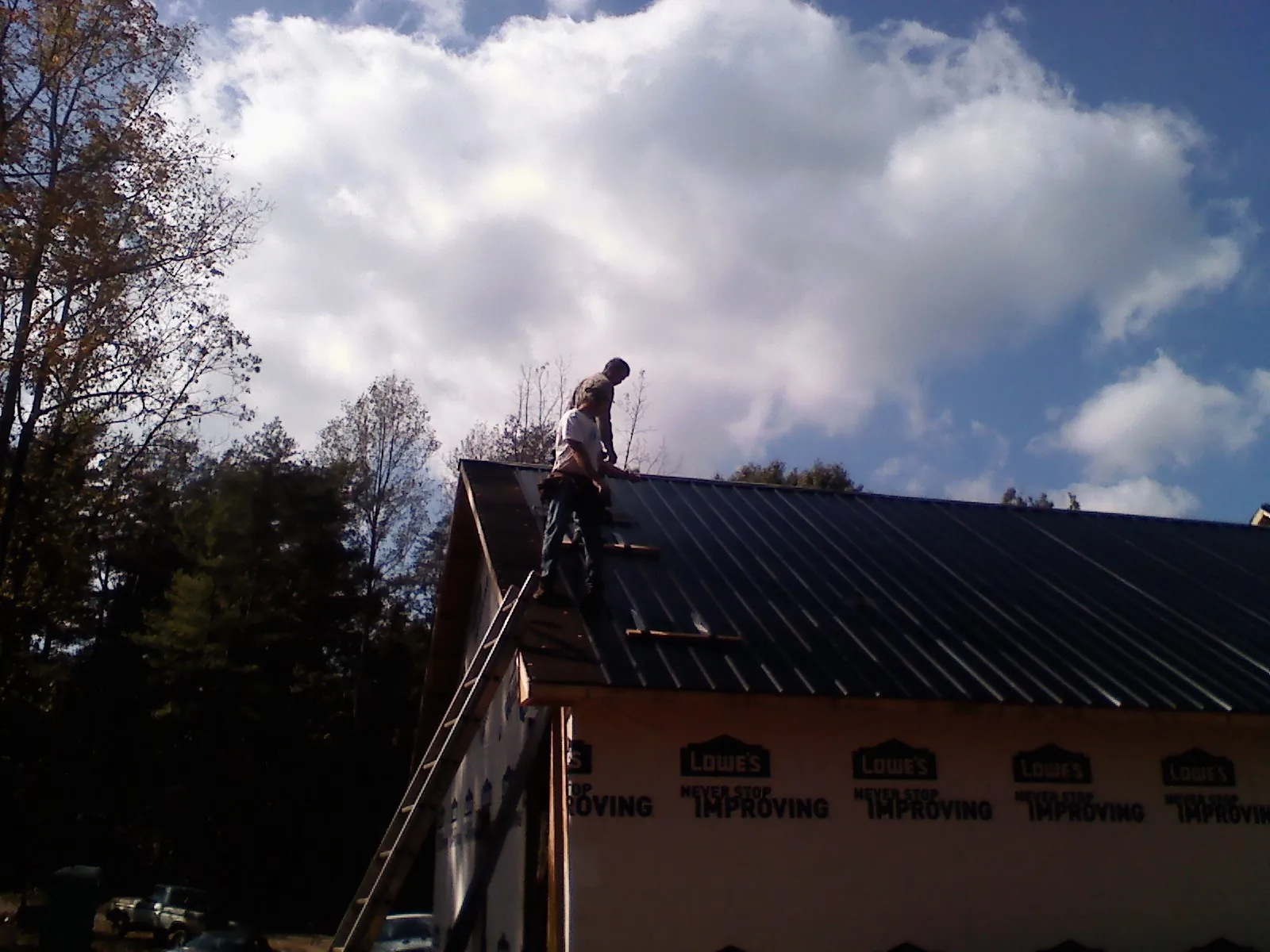 Roofer fastening dark metal panels high against a cloudy sky, from a Roof Inspection job in Cranesville