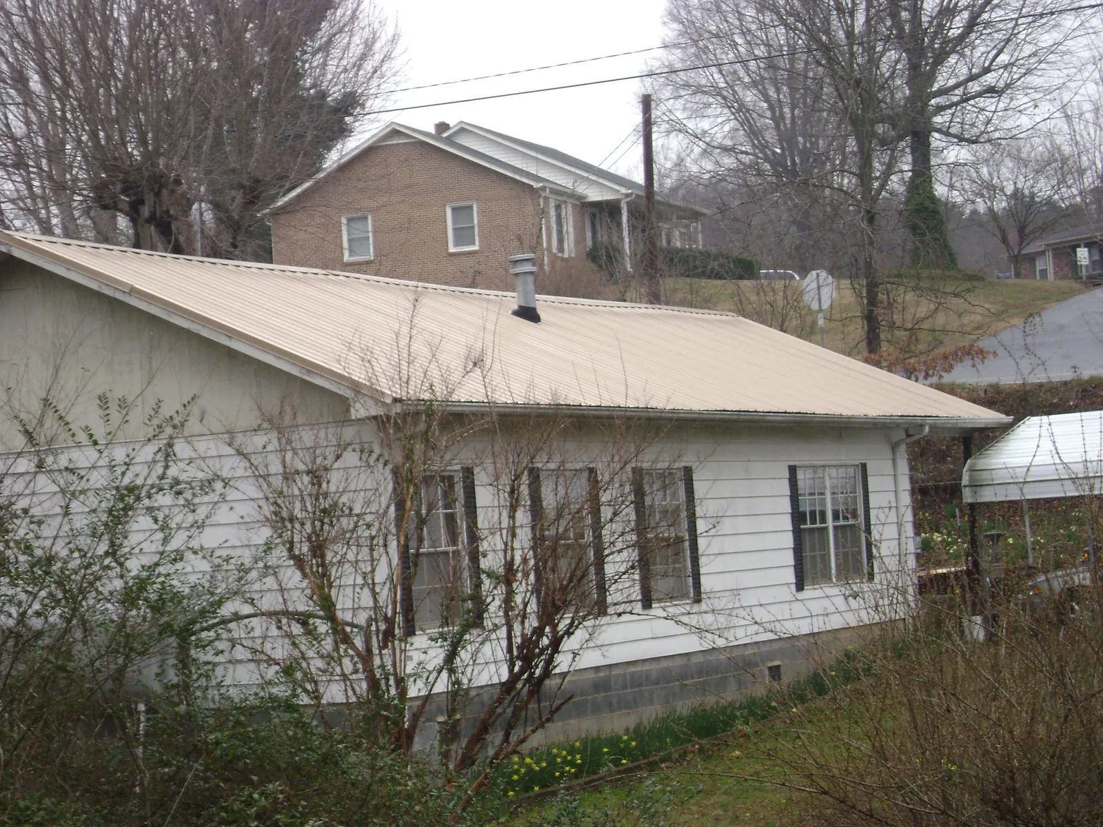Tan metal roof on a white sided house set into a hillside — Commercial Roofing by Roofing Brothers in Cranesville