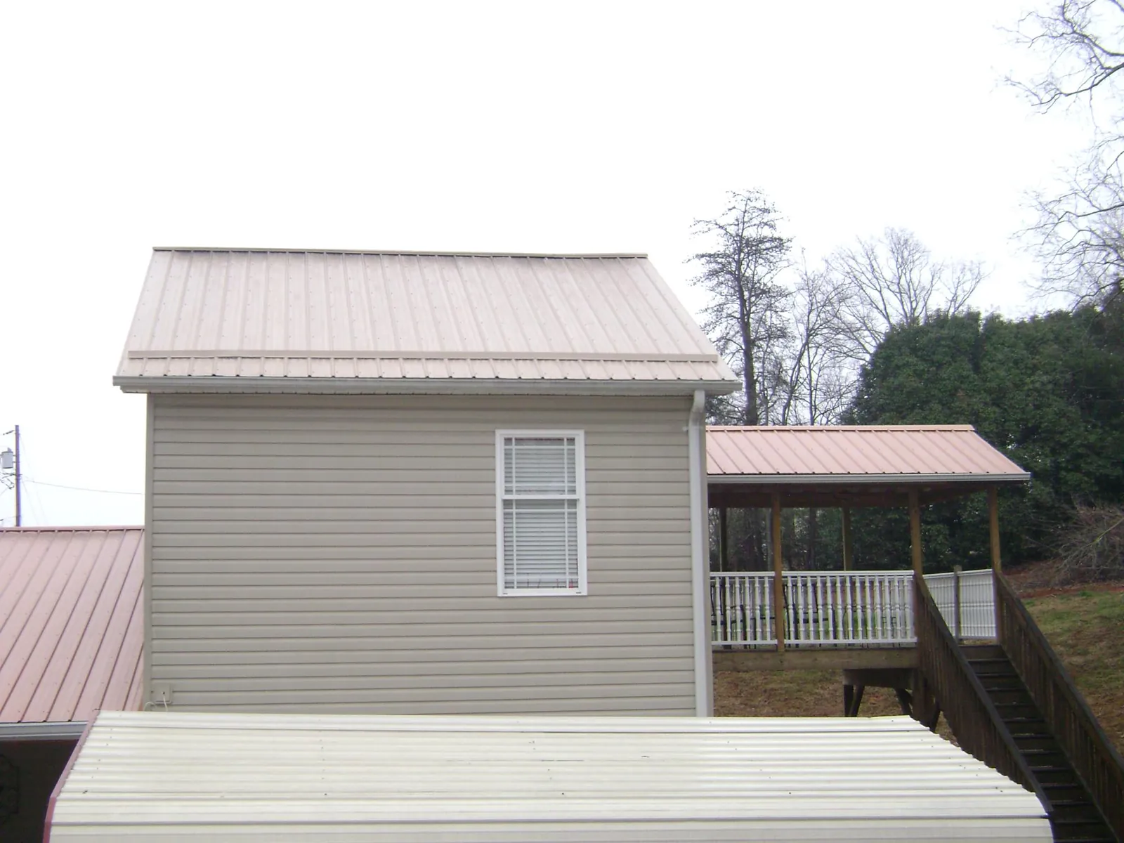 Tan metal roofs on a two story addition and attached porch, from a Roof Replacement job in Cranesville
